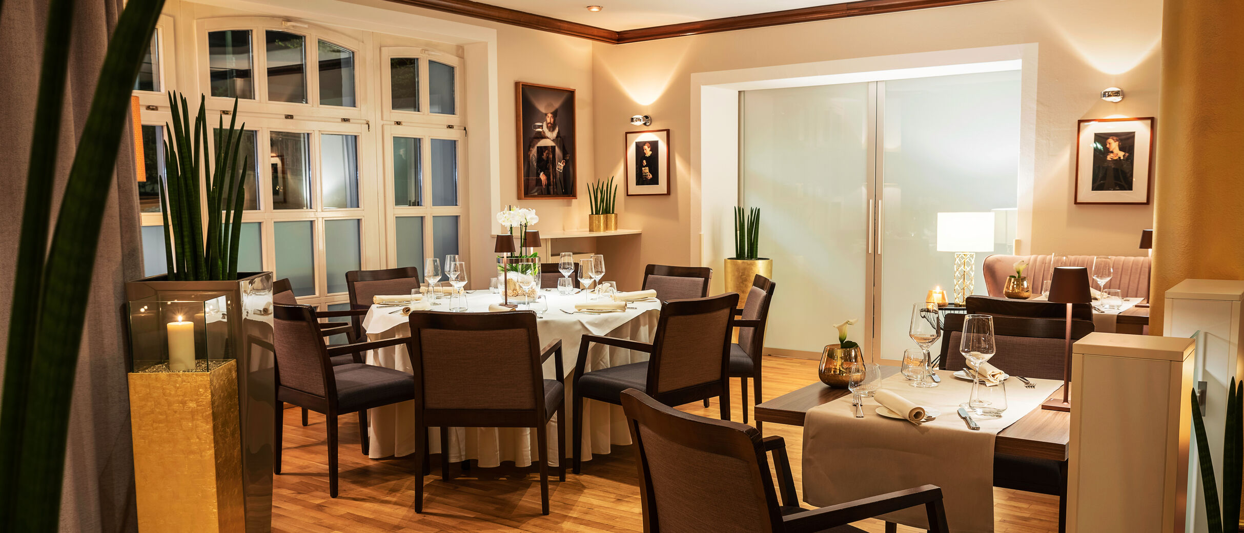 Eine Empore im Restaurant, mit einem runden Tisch, der in sanftem Licht erstrahlt. Die abendliche Stimmung wird durch warmes Licht und eine gemütliche Atmosphäre verstärkt, während der Raum elegant und einladend wirkt.