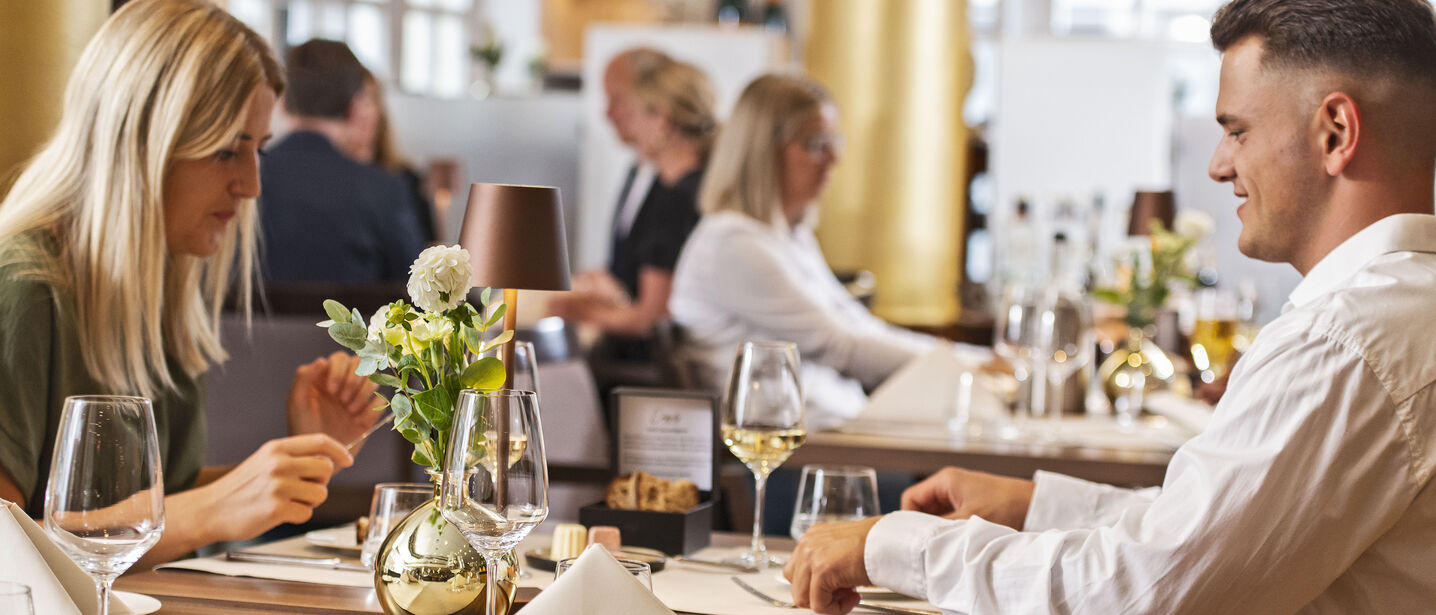 Ein Pärchen genießt ein Menü im Restaurant Engels in der Burg. Im Hintergrund sitzen weitere Gäste in stilvollem Ambiente und genießen ihr Essen.