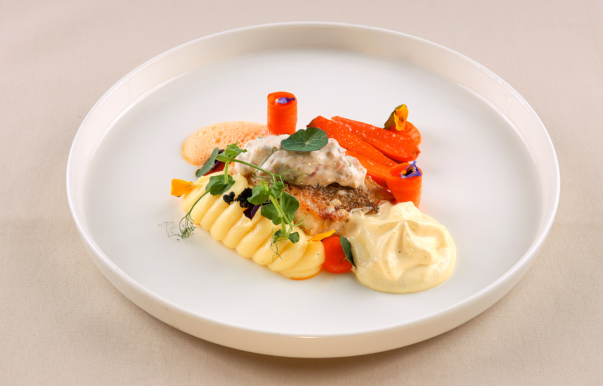 Filet vom Red Snapper mit Nordseekrabben. Serviert mit jungen Möhren, einer feinen Kartoffelbordüre, luftigem Béarnaise-Espuma und aromatischem Krustentierschaum.