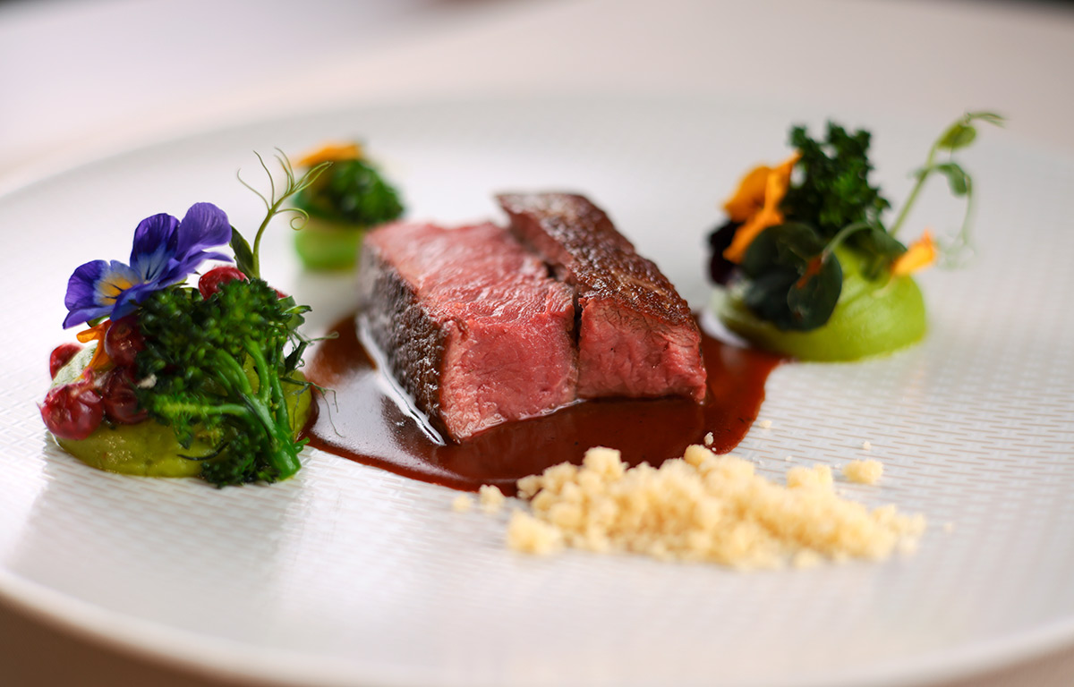 Ein Gericht mit zartem Salzwiesenlamm, serviert mit cremigem Spinatpüree, fruchtigen Preiselbeeren und knackigem wildem Broccoli auf einem eleganten Teller.